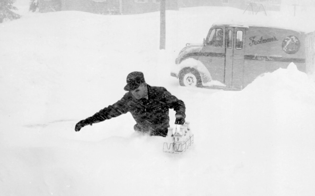 A man struggling through waist-deep snow to deliver milk to Bangor residents during the 1962 blizzard.